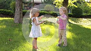 Two fun little kids, a boy and a girl, are playing with soap bubbles in the Park