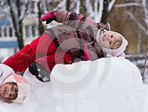 Two funny adorable little sisters building a snowman together in