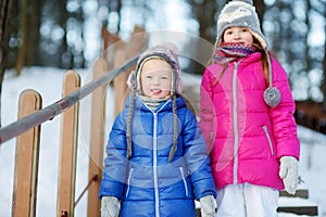 Two funny adorable little sisters having fun together in winter park