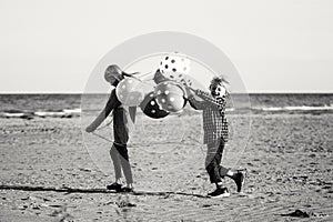 Two funny Caucasian children kids with bunch of balloons playing running on beach