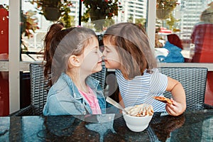 Two funny Caucasian little preschool sisters siblings eat dessert play in cafe.