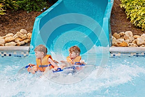 Two funny excited children enjoying summer vacation in water amusement park riding on slide with float. Happy little