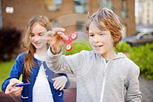 Two funny friends playing with fidget spinners on the playground. Popular stress-relieving toy for school kids and adults.