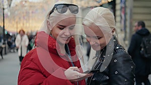 Two funny friends taking selfie outdoors in the street at sunset with a warm light in the background, girls sisters with