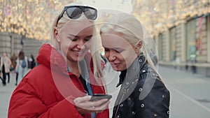 Two funny friends taking selfie outdoors in the street at sunset with a warm light in the background, girls sisters with