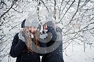 Two funny girls friends having fun at winter snowy day near snow covered trees