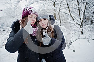 Two funny girls friends having fun at winter snowy day near snow covered trees