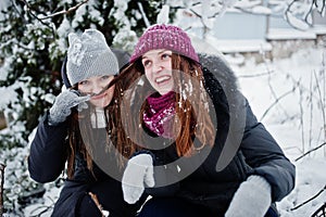 Two funny girls friends having fun at winter snowy day near snow covered trees