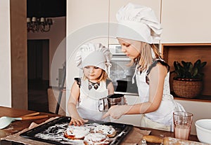 Two funny girls in the kitchen wearing a chef`s hat and white apron playing in the kitchen