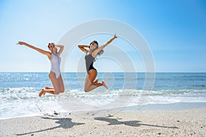 Two funny girls in swimsuit jumping on a tropical beach