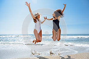 Two funny girls in swimsuit jumping on a tropical beach