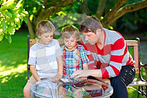 Two funny handsome kid boys and young father playing together checkers game. Sons, siblings children and dad spending