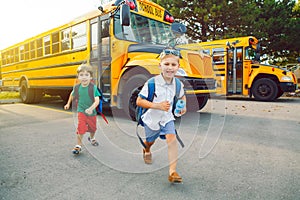 Two funny happy Caucasian boys students kids near yellow bus on 1 September day