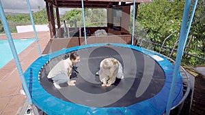 Two funny happy women are jumping on trampoline jokingly, sitting like frogs, smiling and laughing in daytime