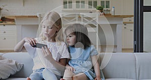 Two funny kids sisters using smartphone taking selfie at home