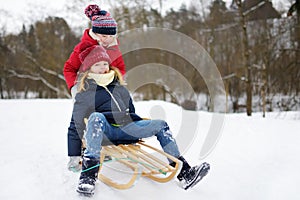 Two funny little girls having fun with a sleigh in beautiful winter park. Cute children playing in a snow.