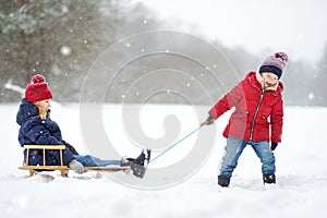 Two funny little girls having fun with a sleigh in beautiful winter park. Cute children playing in a snow.