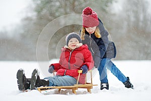 Two funny little girls having fun with a sleigh in beautiful winter park. Cute children playing in a snow.