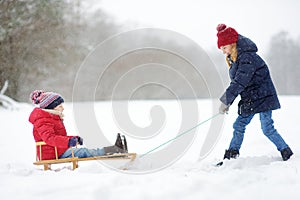 Two funny little girls having fun with a sleigh in beautiful winter park. Cute children playing in a snow.