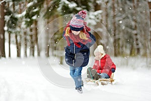 Two funny little girls having fun with a sleigh in beautiful winter park. Cute children playing in a snow.