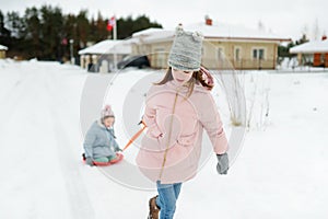 Two funny little girls having fun with a sleigh in beautiful winter park. Cute children playing in a snow