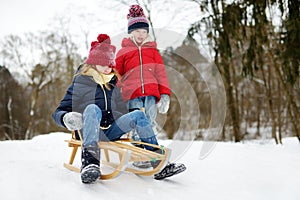 Two funny little girls having fun with a sleigh in beautiful winter park. Cute children playing in a snow.