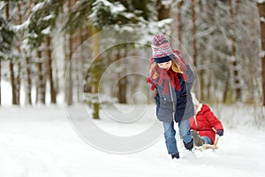 Two funny little girls having fun with a sleigh in beautiful winter park. Cute children playing in a snow.