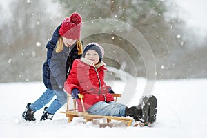 Two funny little girls having fun with a sleigh in beautiful winter park. Cute children playing in a snow.