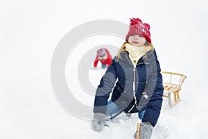 Two funny little girls having fun with a sleigh in beautiful winter park. Cute children playing in a snow.