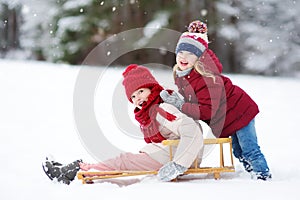 Two funny little girls having fun with a sleight in beautiful winter park. Cute children playing in a snow.