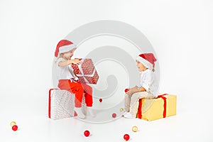 Two funny little kids in Santa hat sitting on gift boxes. Isolated on white background. Christmas and new year concept