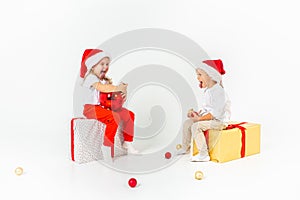 Two funny little kids in Santa hat sitting on gift boxes. Isolated on white background. Christmas and new year concept