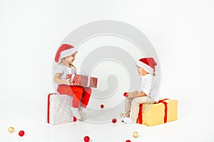 Two funny little kids in Santa hat sitting on gift boxes. Isolated on white background. Christmas and new year concept