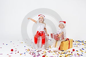 Two funny little kids in Santa hat sitting on gift boxes. Isolated on white background, confetti on a floor. Christmas and new