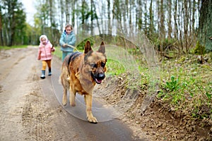 Two funny little sisters walking their dog on a forest hike