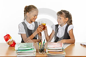 Two funny schoolgirls at a table drink juice, and banged glasses photo