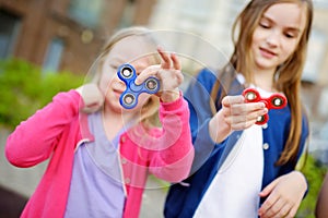 Two funny sisters playing with fidget spinners on the playground. Popular stress-relieving toy for school kids and adults.