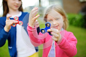 Two funny sisters playing with fidget spinners on the playground. Popular stress-relieving toy for school kids and adults.