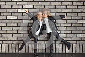 Two funny sisters in same outfits: white t-shirts, leather black jackets and leggings