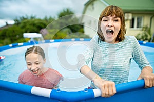 Two funny teenage sisters trying to get into cold pool water. Children having fun in outdoor pool. Summer activities for the