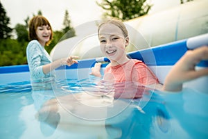 Two funny teenage sisters trying to get into cold pool water. Children having fun in outdoor pool. Summer activities for the