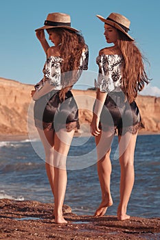 Two funny twins girl in straw hat having fun on the beach enjoying life, summer sunset outdoor portrait. People Girlfriend freedom