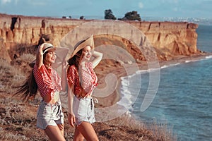 Two funny twins girl in straw hat having fun cliff mountains enjoying lagoon in summer sunset outdoor portrait. People Girlfriend