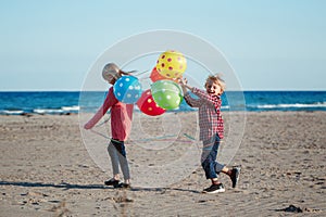 Two funny white Caucasian children kids with colorful bunch of balloons, playing running on beach on sunset, autumn summer