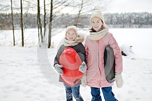 Two funny young girls having fun with a sleigh in beautiful winter park. Cute children playing in a snow