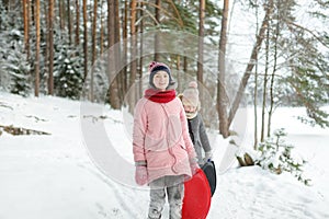 Two funny young girls having fun with a sleigh in beautiful winter park. Cute children playing in a snow