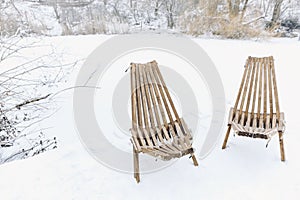 Two garden chairs with white lambskin outside on a wooden deck by the lake. After ski outside in the snow. Sitting outside in