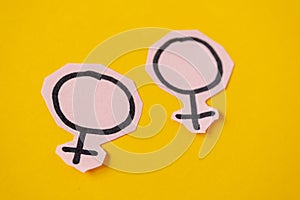 Two gender symbols Venus cut from pink paper on yellow background. Concept lgbt