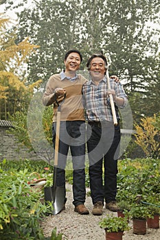 Two generation working in garden, smiling and holding gardening tools