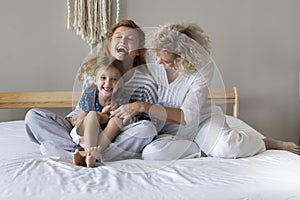 Two generations of women tickling little girl seated on bed